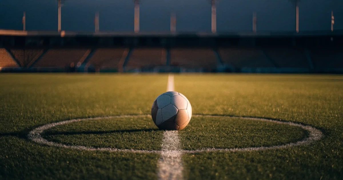 Ein Fussball liegt auf dem Mittelkreis eines Rasenfelds, die weissen Linien kreuzen sich auf dem gepflegten Gras im warmen Abendlicht.