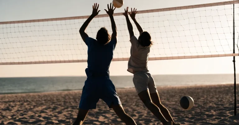 Ein Volleyball liegt auf feinem hellem Sand, ein gespanntes Netz verschwimmt dahinter, das Licht kommt von einem weiten Meer.