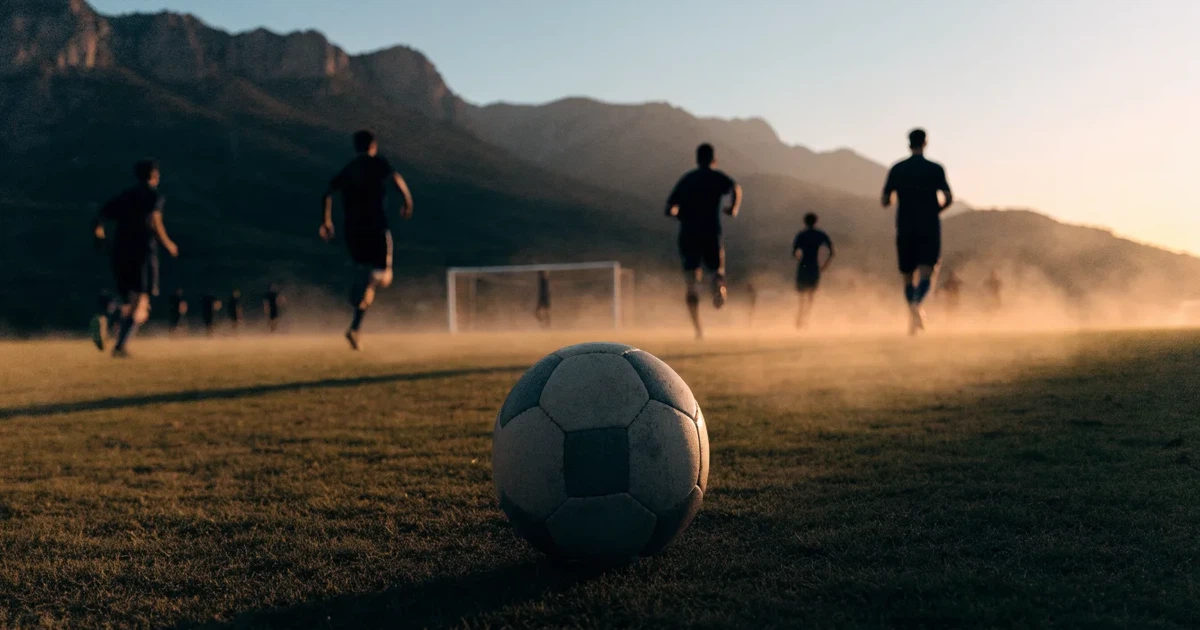 Ein Fussball auf einem staubigen Rasenstück in der Abendsonne, im Hintergrund eine hohe Bergkette